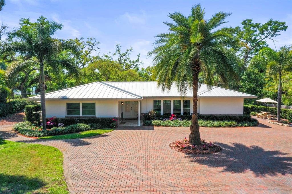 A single-story house with a white exterior and metal roof sits behind a brick driveway — 1600 PARK STREET N, ST PETERSBURG, FL