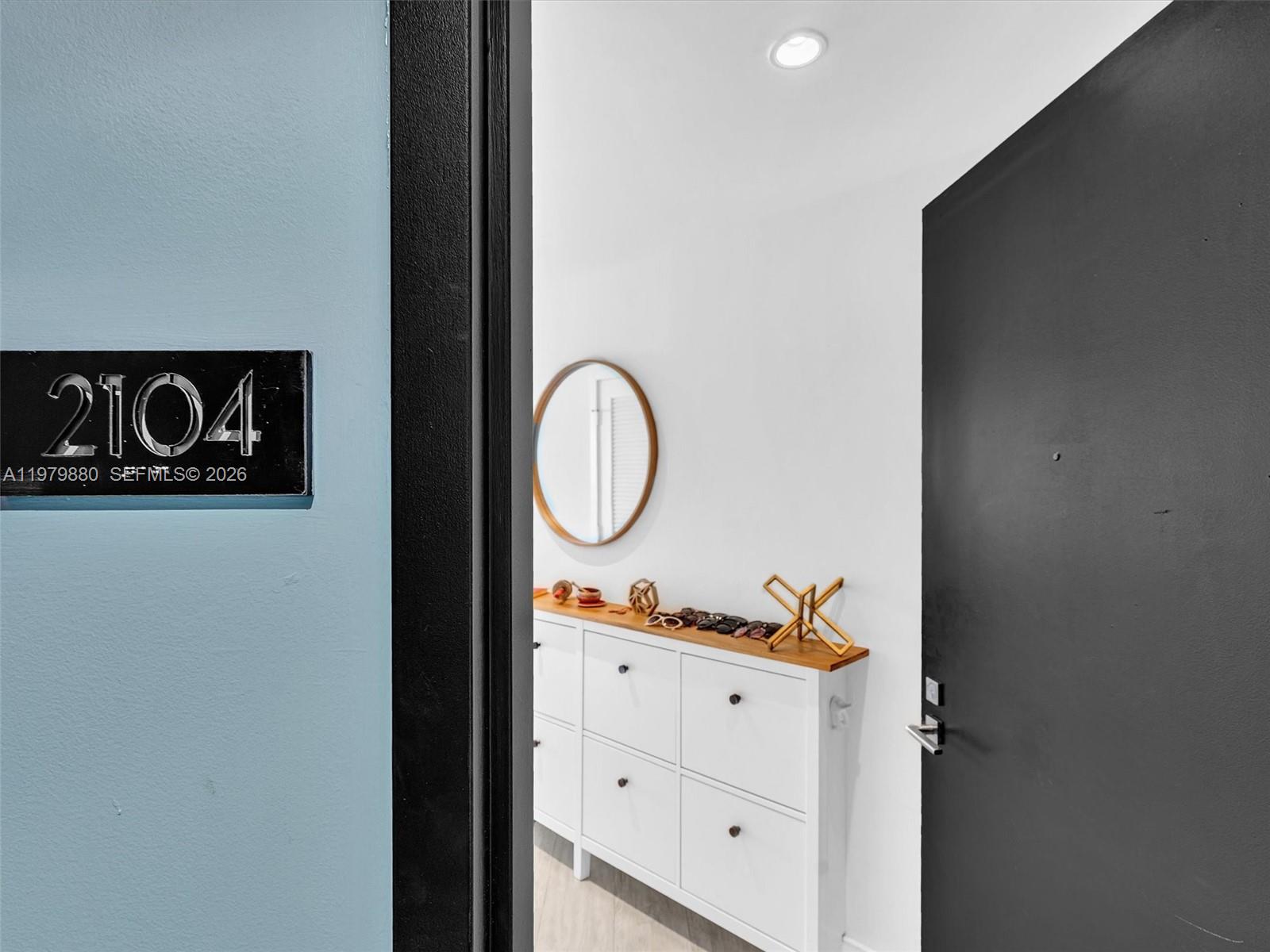 A white shoe cabinet sits in an entryway with a round mirror on the wall — 121 NE 34th St # 2104, Miami FL 33137, MIAMI, FL