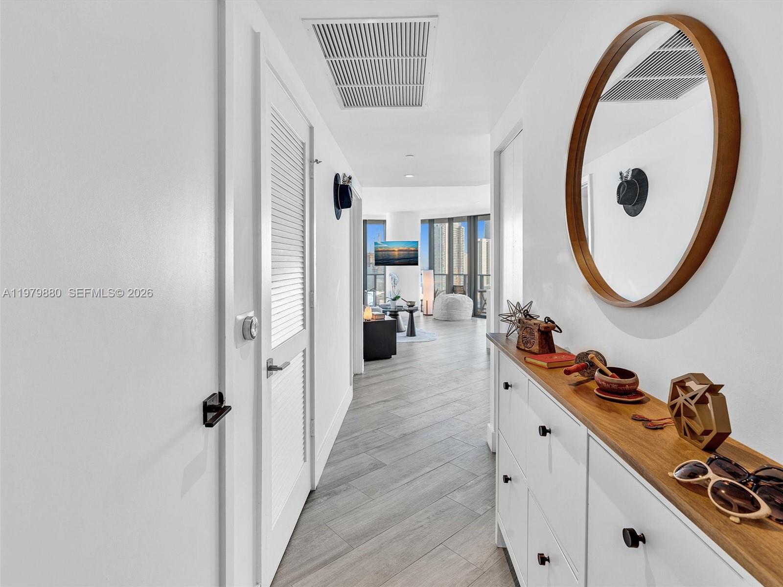 A hallway with white walls, wood-look tile flooring, a wooden console table, and a mirror — 121 NE 34th St # 2104, Miami FL 33137, MIAMI, FL