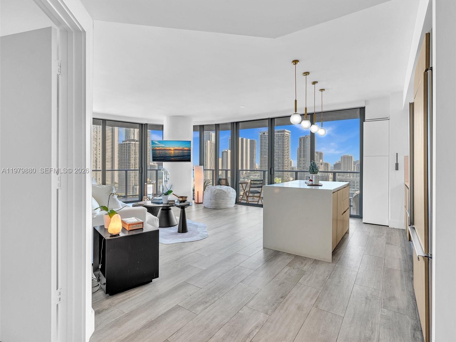 A modern open-concept living area features a kitchen island, floor-to-ceiling windows, and city views — 121 NE 34th St # 2104, Miami FL 33137, MIAMI, FL