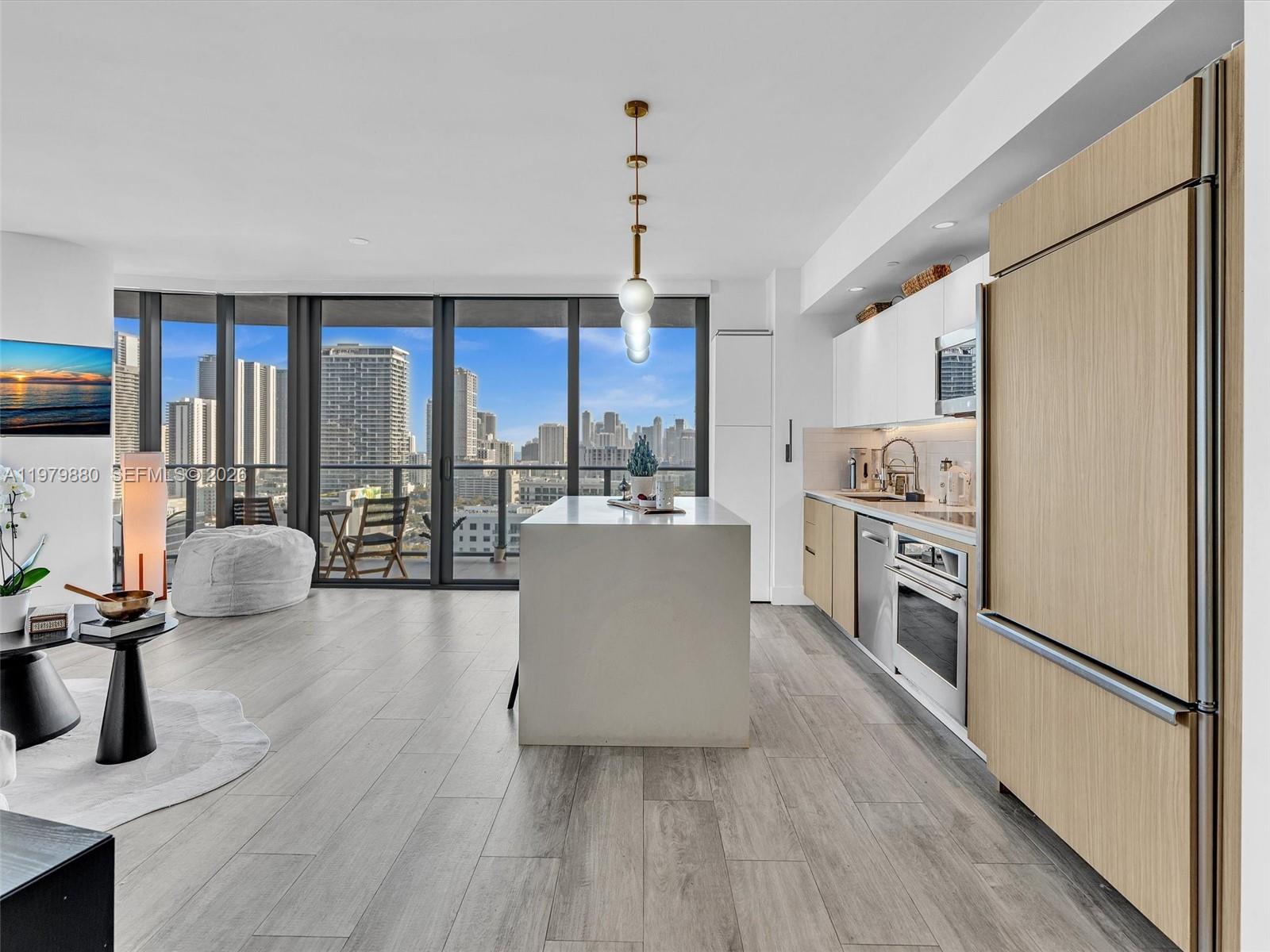 A modern kitchen and living area feature light wood cabinetry, a central island, and floor-to-ceiling windows — 121 NE 34th St # 2104, Miami FL 33137, MIAMI, FL