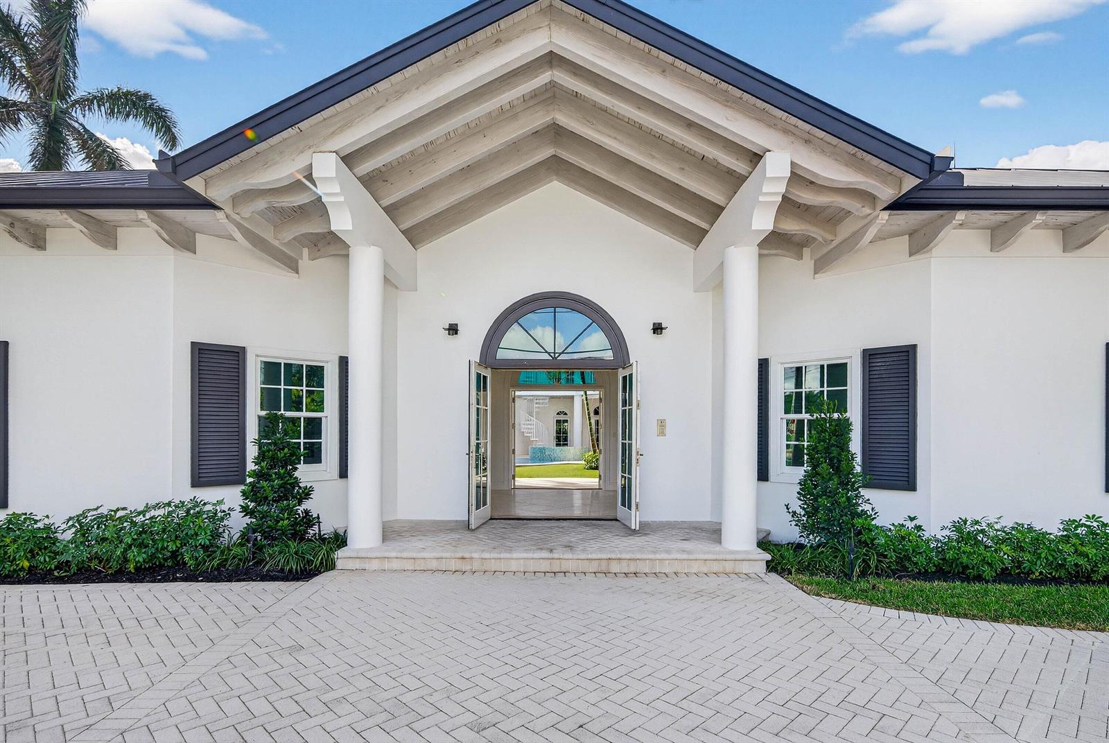 The exterior of a white house features a gabled entryway with columns and double doors — 720 N Ocean Boulevard, Delray Beach FL 33483, DELRAY BEACH, FL
