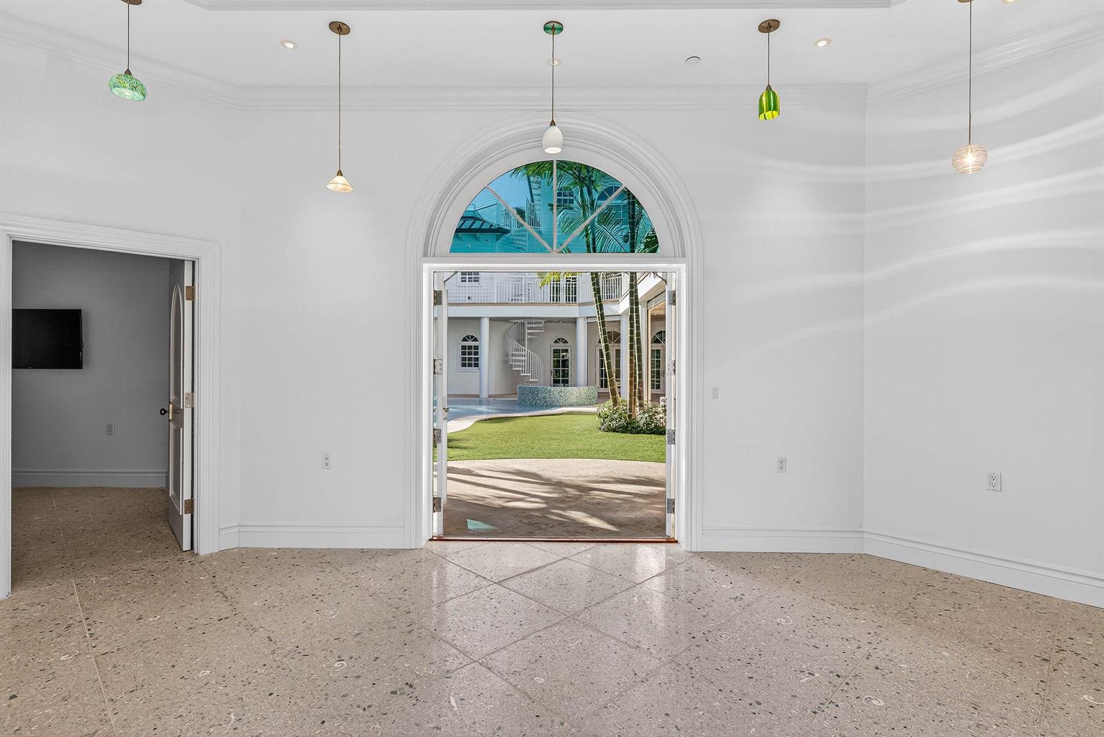 A bright room with terrazzo floors features a large arched doorway opening to a courtyard — 720 N Ocean Boulevard, Delray Beach FL 33483, DELRAY BEACH, FL