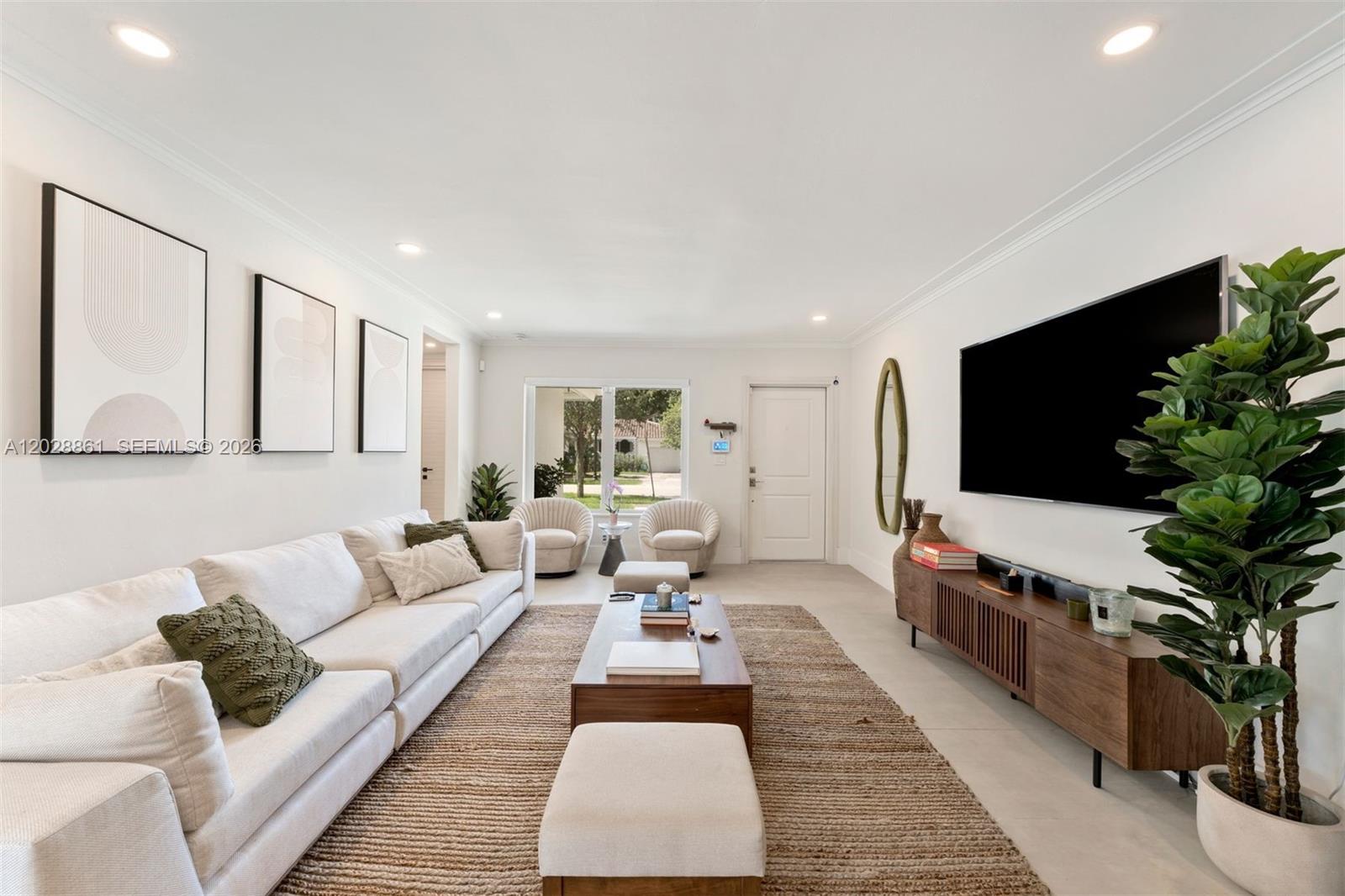 A bright living room features a white sofa, a wooden coffee table, and a television — 45 Palermo Ave, Coral Gables FL 33134, CORAL GABLES, FL