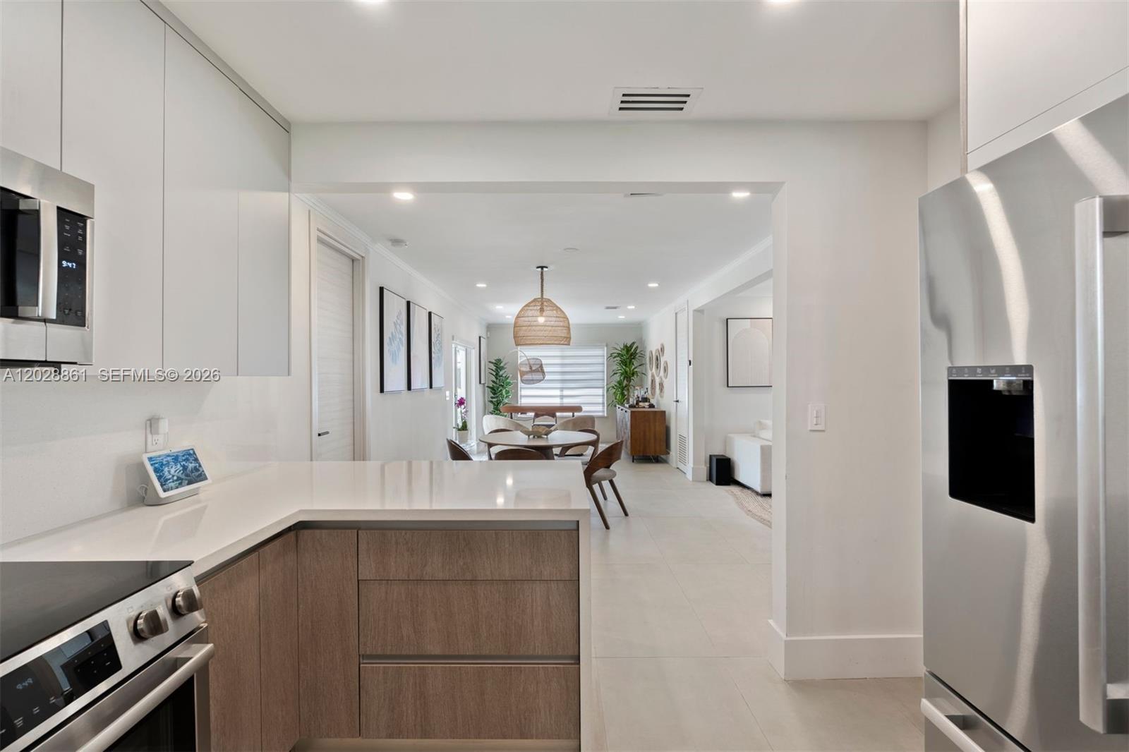 A modern kitchen with wood-toned cabinets and white countertops opens into a dining area — 45 Palermo Ave, Coral Gables FL 33134, CORAL GABLES, FL