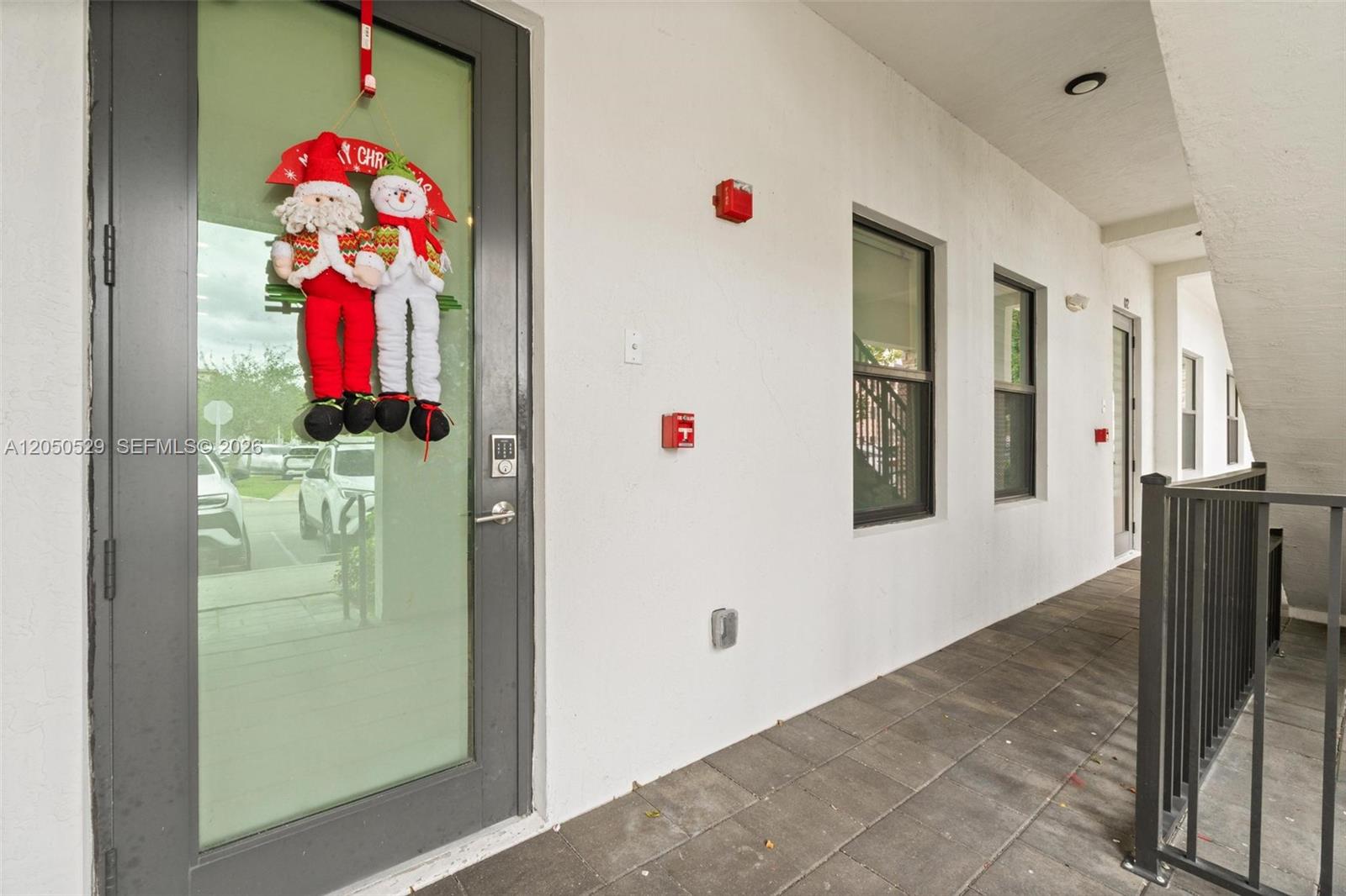 A gray door with a holiday decoration opens onto a tiled outdoor walkway — 7809 NW 104th Ave # 1, Doral FL 33178, DORAL, FL