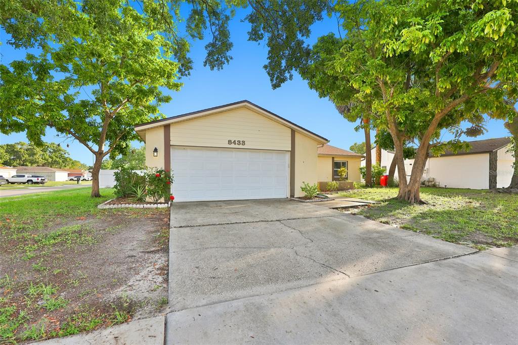 A single-story house with a beige exterior, a two-car garage, and mature trees in front — 8433 SOMERSET DRIVE, LARGO, FL
