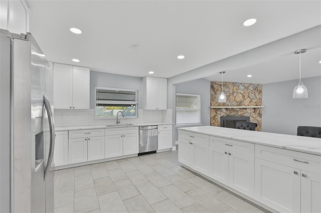 A modern kitchen features white cabinets, stainless steel appliances, a large island, and stone fireplace — 8433 SOMERSET DRIVE, LARGO, FL