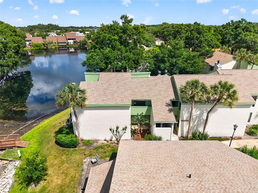 An aerial view shows a multi-story residential building with a shingled roof beside a lake — 13405 PINE LAKE WAY UNIT 203, TAMPA, FL
