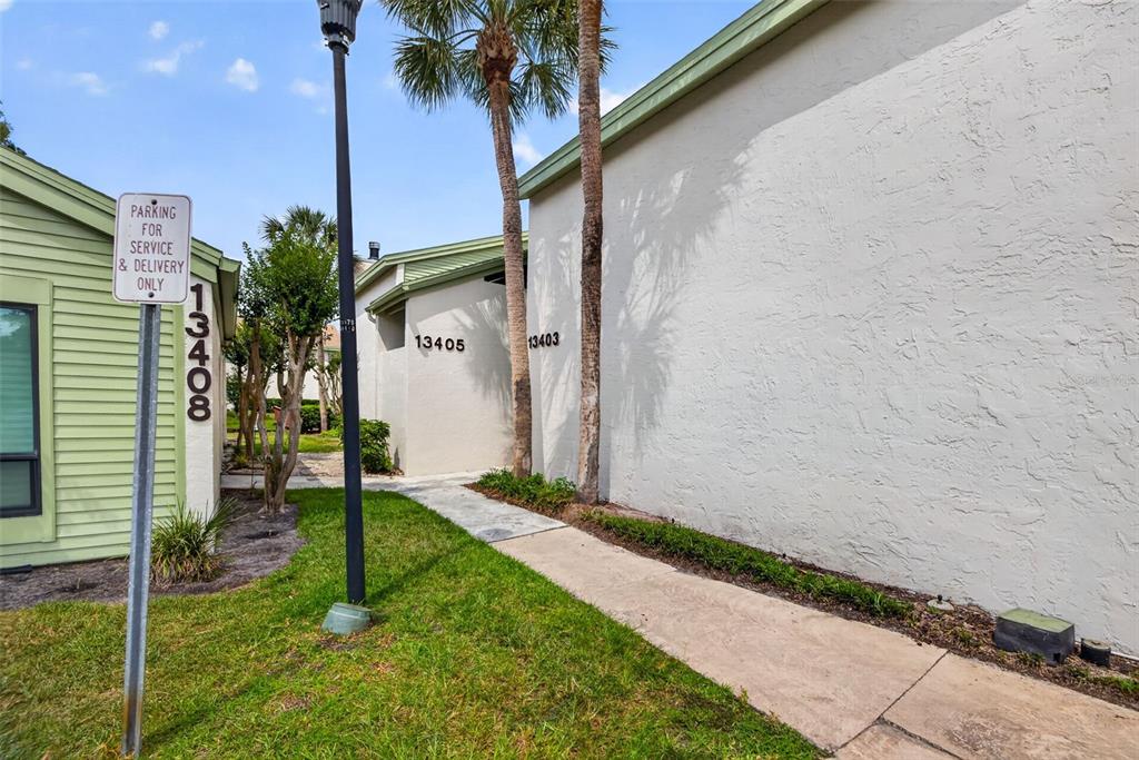 A sidewalk leads between two exterior building walls marked with unit numbers and palm trees — 13405 PINE LAKE WAY UNIT 203, TAMPA, FL