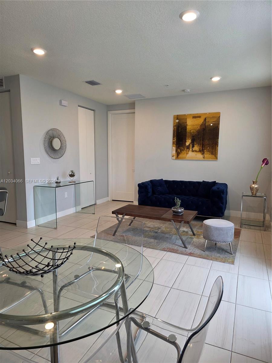 A living and dining area features a blue tufted sofa, glass tables, and tile flooring — 10222 NW 64th Way # 302, Doral FL 33178, DORAL, FL