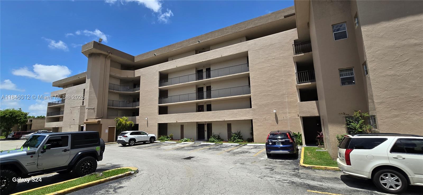 The exterior of a multi-story tan apartment building features balconies and a parking lot — 816 NW 87th Ave # 107, Miami FL 33172, MIAMI, FL