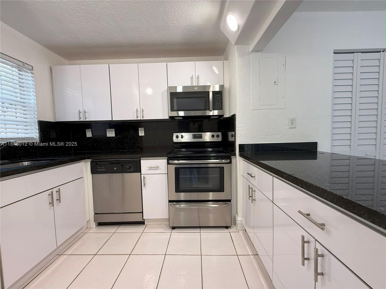 A kitchen features white cabinets, black countertops, stainless steel appliances, and white tile flooring — 816 NW 87th Ave # 107, Miami FL 33172, MIAMI, FL