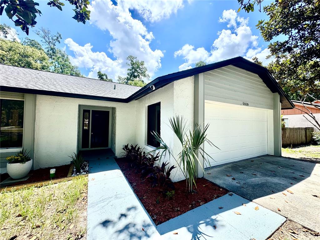 A white stucco house features a front-facing garage, a paved walkway, and a landscaped garden — 5509 LIGHTHOUSE ROAD, ORLANDO, FL