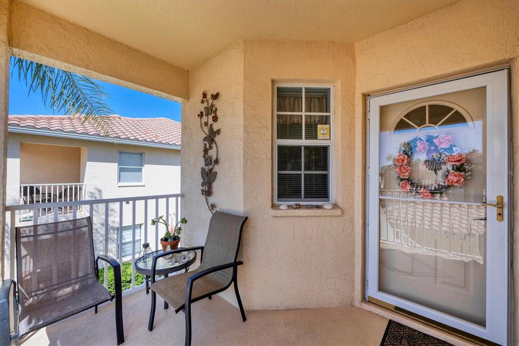 A covered balcony features two chairs, a small table, a window, and a screen door — 4206 VICENZA DRIVE UNIT C24, VENICE, FL