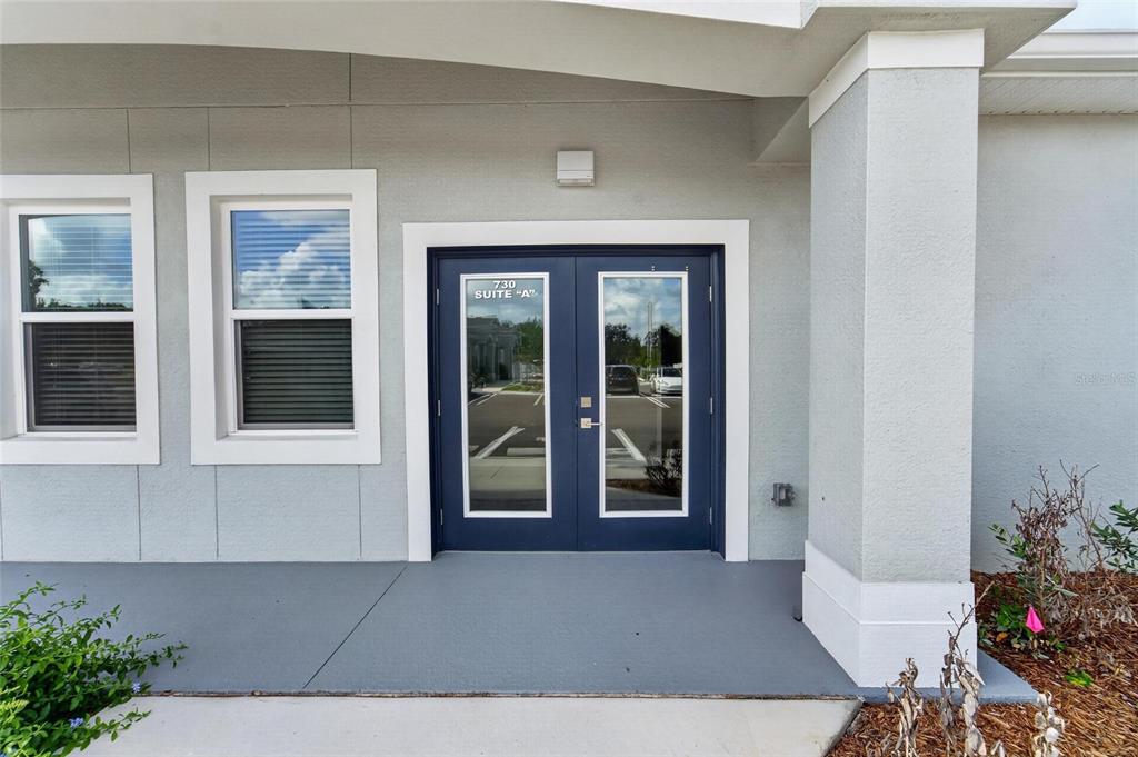 A gray building exterior features a double glass door labeled Suite A under a porch — 730 CACTUS RIDGE CIRCLE UNIT A, SEFFNER, FL