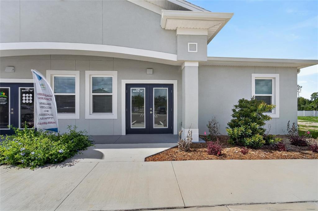 The exterior of a commercial building features a concrete walkway, double doors, and landscaping — 730 CACTUS RIDGE CIRCLE UNIT A, SEFFNER, FL