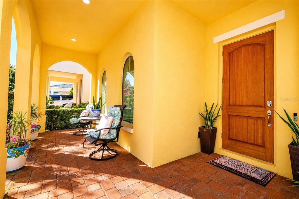 A covered brick porch features yellow walls, arched windows, patio furniture, and a wooden door — 15149 CANOE PLACE, WINTER GARDEN, FL