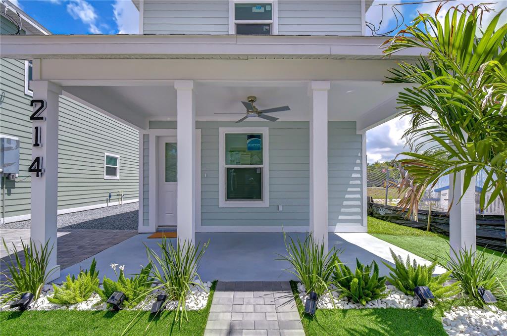A covered front porch with a ceiling fan, light-colored siding, and a paved walkway — 214 8TH AVENUE DRIVE W, BRADENTON, FL