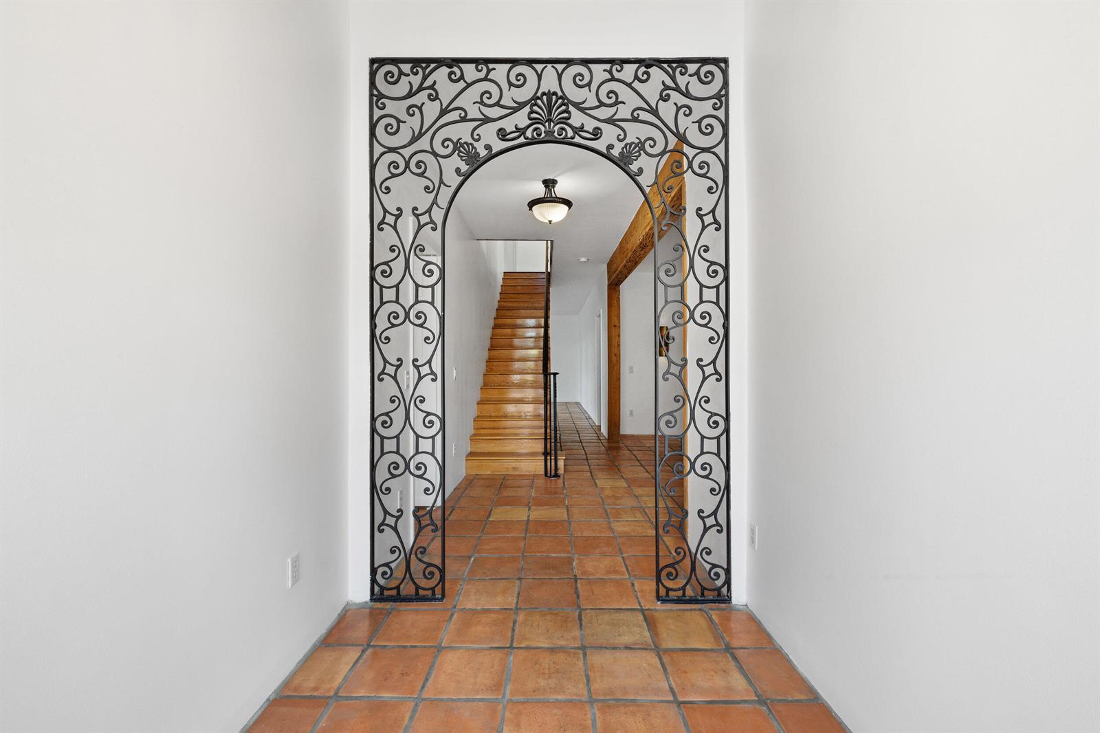 A hallway with terracotta tile flooring features an ornate black wrought iron arched entryway — 269 Park Avenue, Palm Beach FL 33480, PALM BEACH, FL