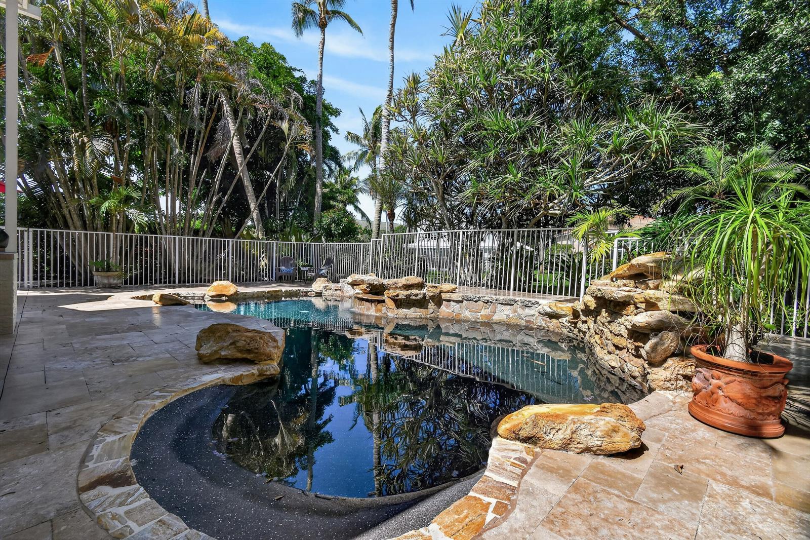 A backyard swimming pool features natural rock accents, a stone patio, and lush tropical landscaping — 276 Swan Lane, Jupiter FL 33458, JUPITER, FL