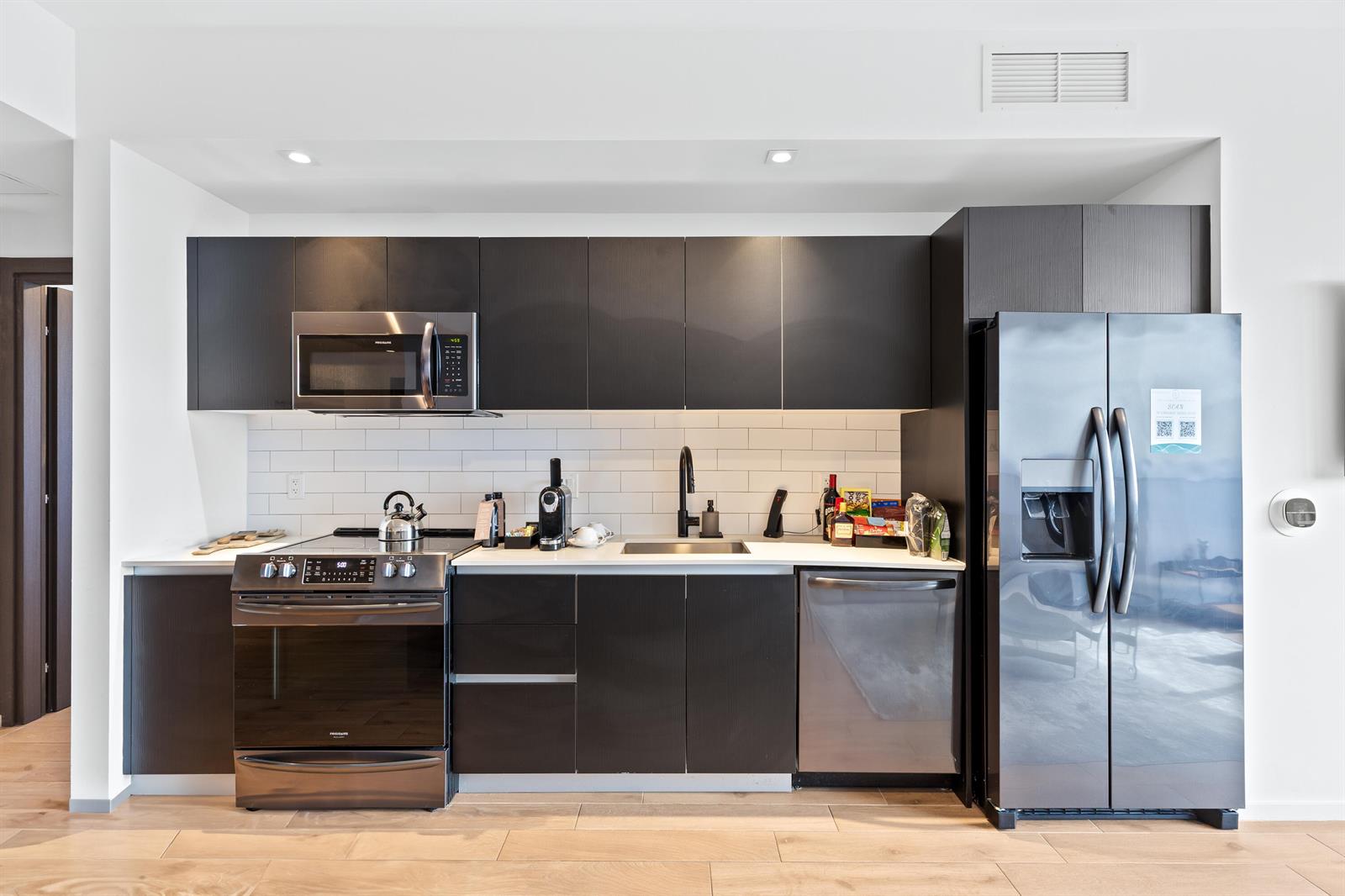 A modern kitchen features dark cabinetry, stainless steel appliances, and a white subway tile backsplash — 398 NE 5th Street # 4618, Miami FL 33132, MIAMI, FL