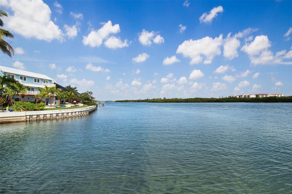 A waterfront view of a house with a seawall, palm trees, and a distant shoreline — 1389 SIESTA BAYSIDE DRIVE UNIT 1389-F, SARASOTA, FL