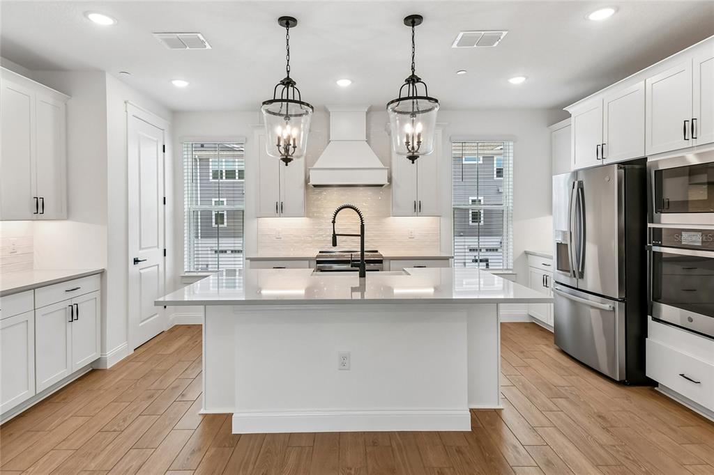 A modern white kitchen features a central island, stainless steel appliances, and two hanging pendants — 230 PASQUALA WAY, OVIEDO, FL