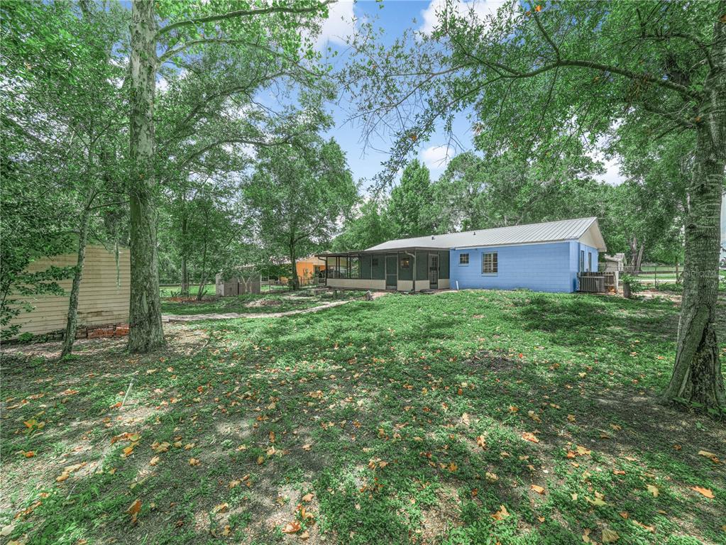 The backyard of a blue house features a screened porch, mature trees, and a shed — 3855 HILL-N-DALE PLACE, LAKELAND, FL