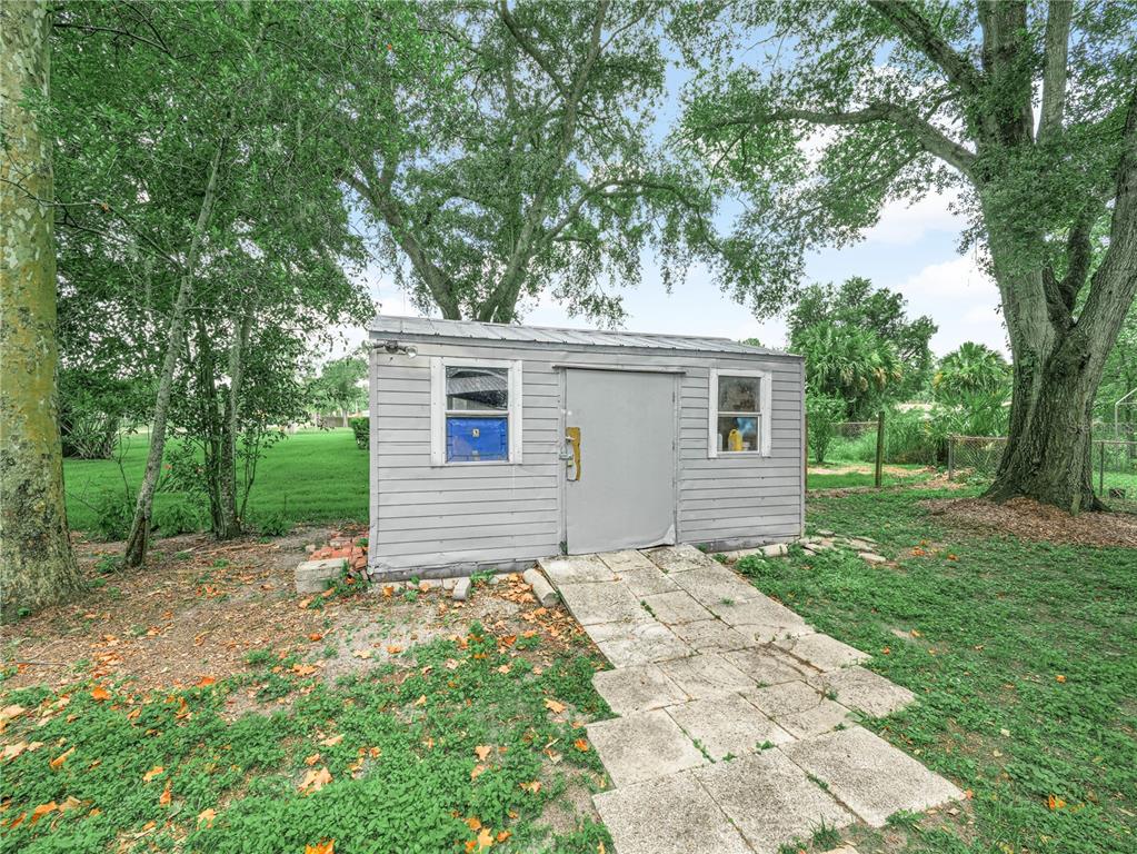 A grey storage shed with a metal door and a stone walkway in a yard — 3855 HILL-N-DALE PLACE, LAKELAND, FL