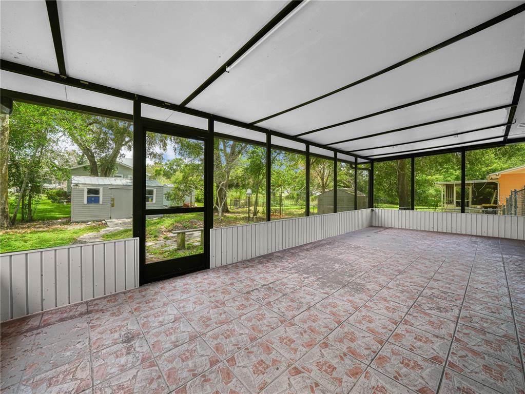 A screened-in porch with tiled flooring, white paneling, and a view of the backyard — 3855 HILL-N-DALE PLACE, LAKELAND, FL