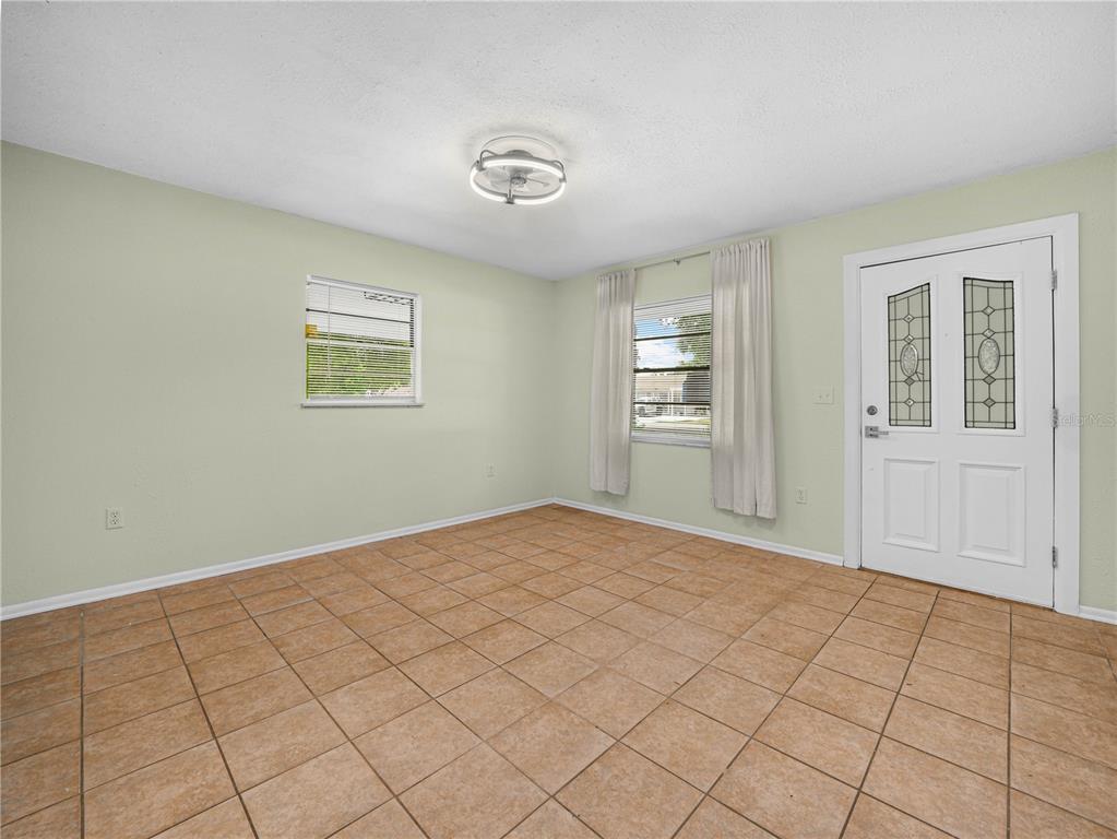An empty room with light green walls, tile flooring, two windows, and a white front door — 3855 HILL-N-DALE PLACE, LAKELAND, FL