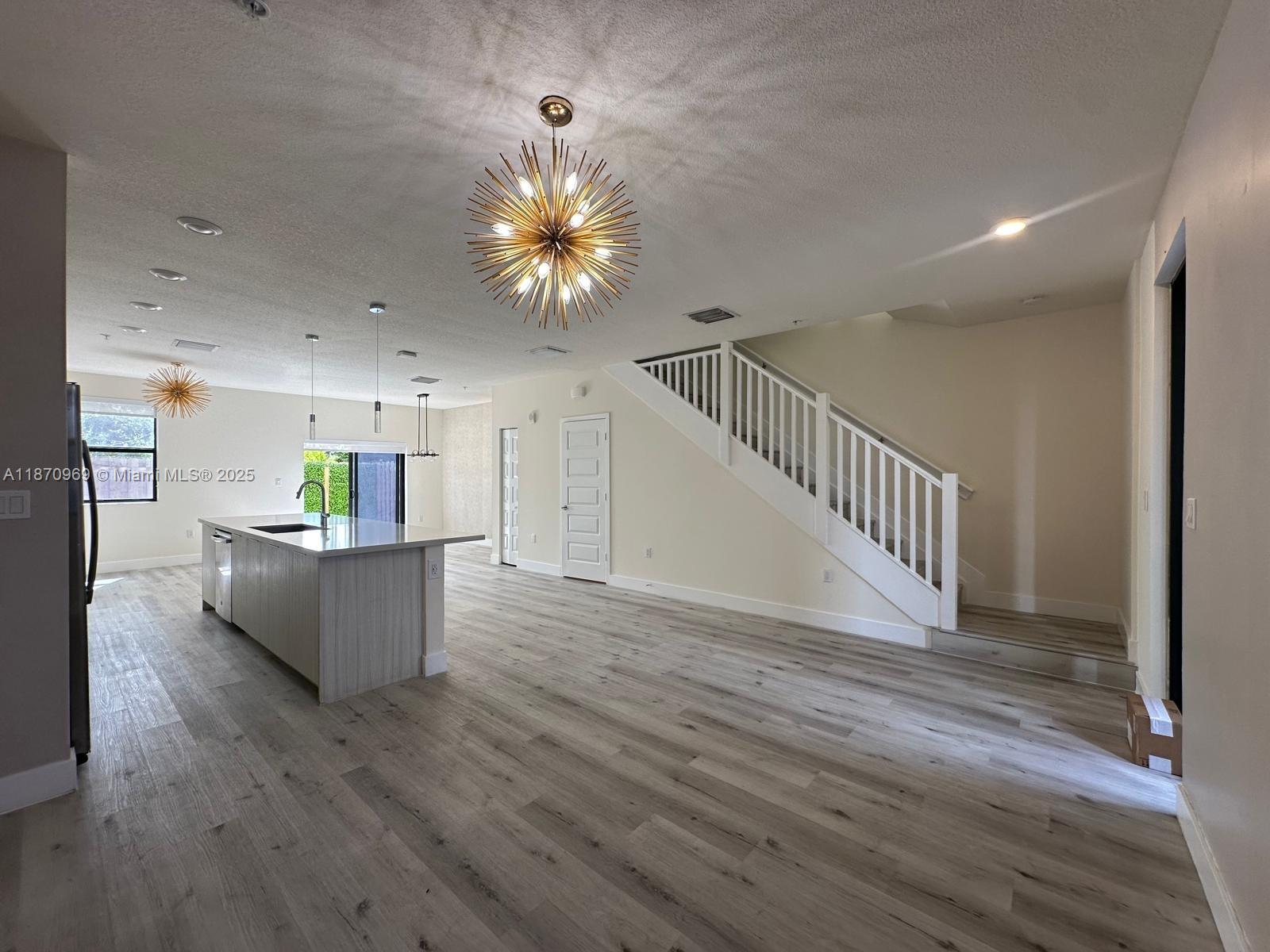 An open-concept kitchen and living area features light wood-look flooring, a central island, and stairs — 10413 NW 82nd St # 9, Doral FL 33178, DORAL, FL
