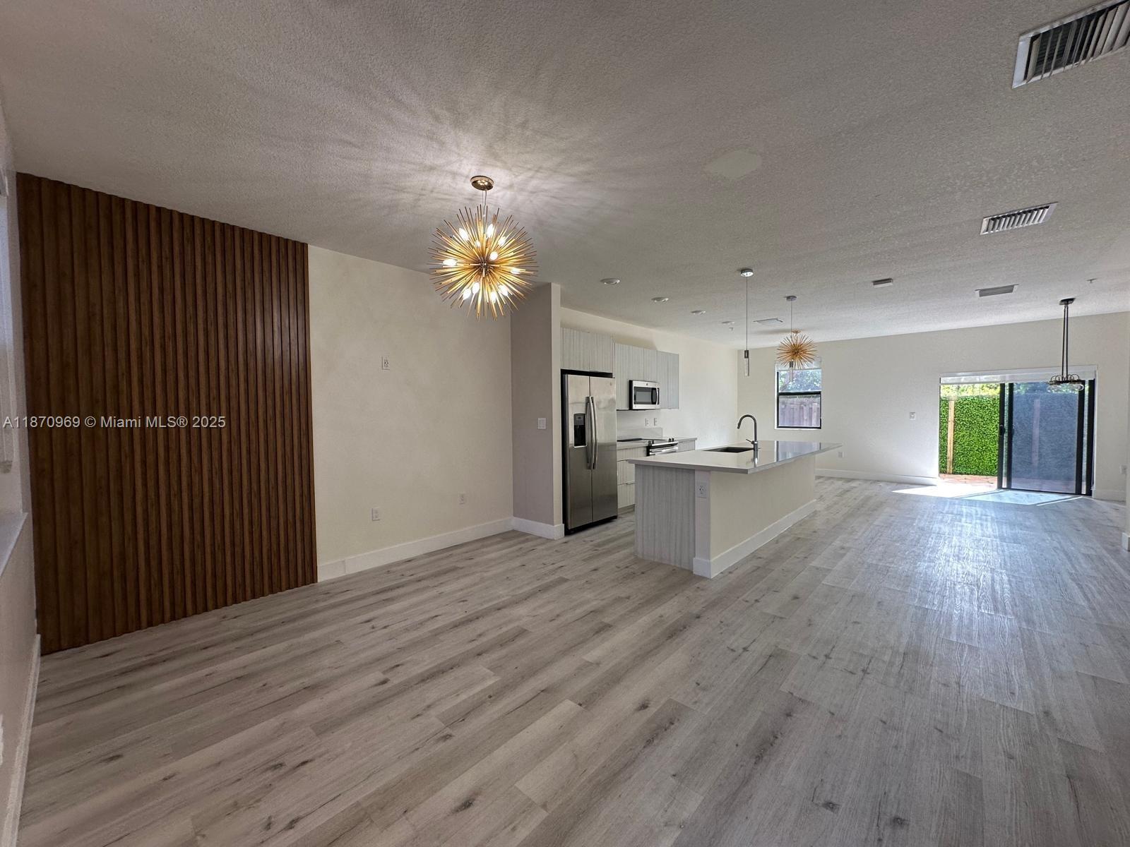 An open-concept kitchen and living area features wood-slat wall paneling and light wood-look flooring — 10413 NW 82nd St # 9, Doral FL 33178, DORAL, FL