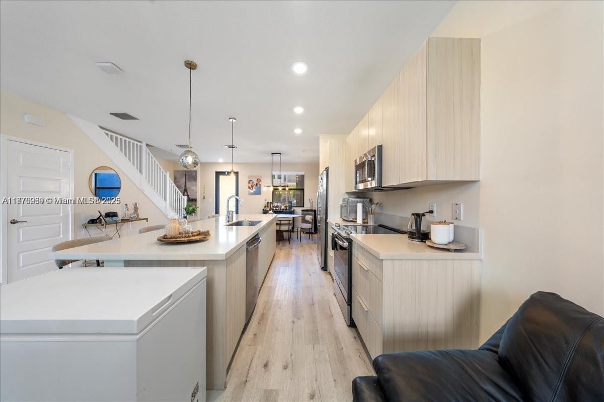 A modern kitchen features light wood cabinetry, white countertops, and an island with seating — 10413 NW 82nd St # 9, Doral FL 33178, DORAL, FL
