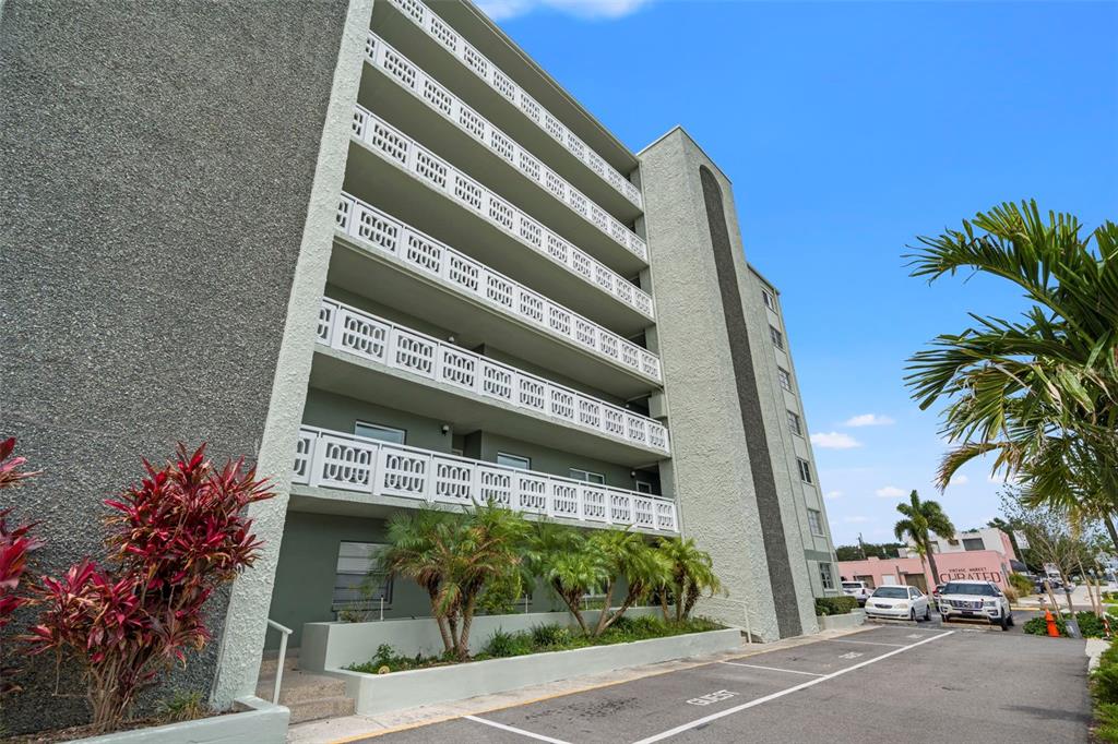 A multi-story apartment building features white decorative balcony railings and a paved parking area — 7321 CENTRAL AVENUE UNIT 407, ST PETERSBURG, FL