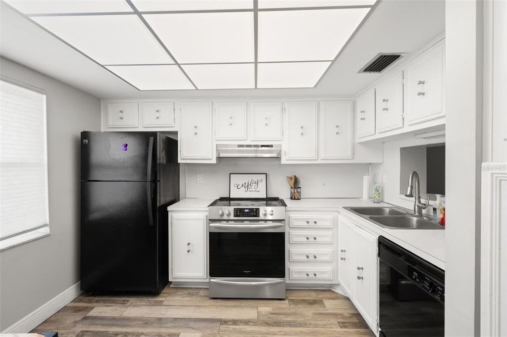 A kitchen features white cabinets, stainless steel appliances, a black refrigerator, and wood-look flooring — 7321 CENTRAL AVENUE UNIT 407, ST PETERSBURG, FL