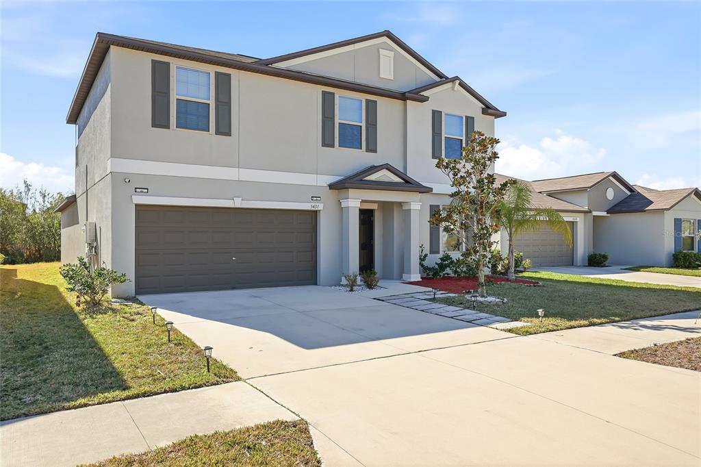 A two-story suburban house with a beige exterior, brown garage door, and concrete driveway — 5431 AMARYLLIS GARDEN STREET, RUSKIN, FL