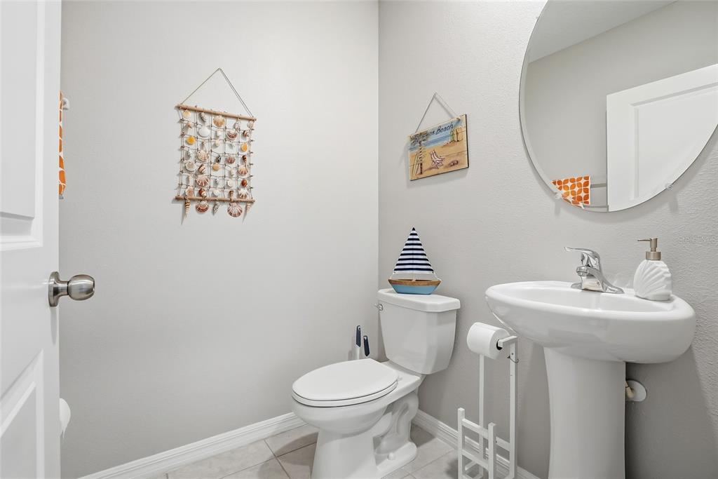 A small bathroom features a pedestal sink, a toilet, and beach-themed wall decor — 5431 AMARYLLIS GARDEN STREET, RUSKIN, FL