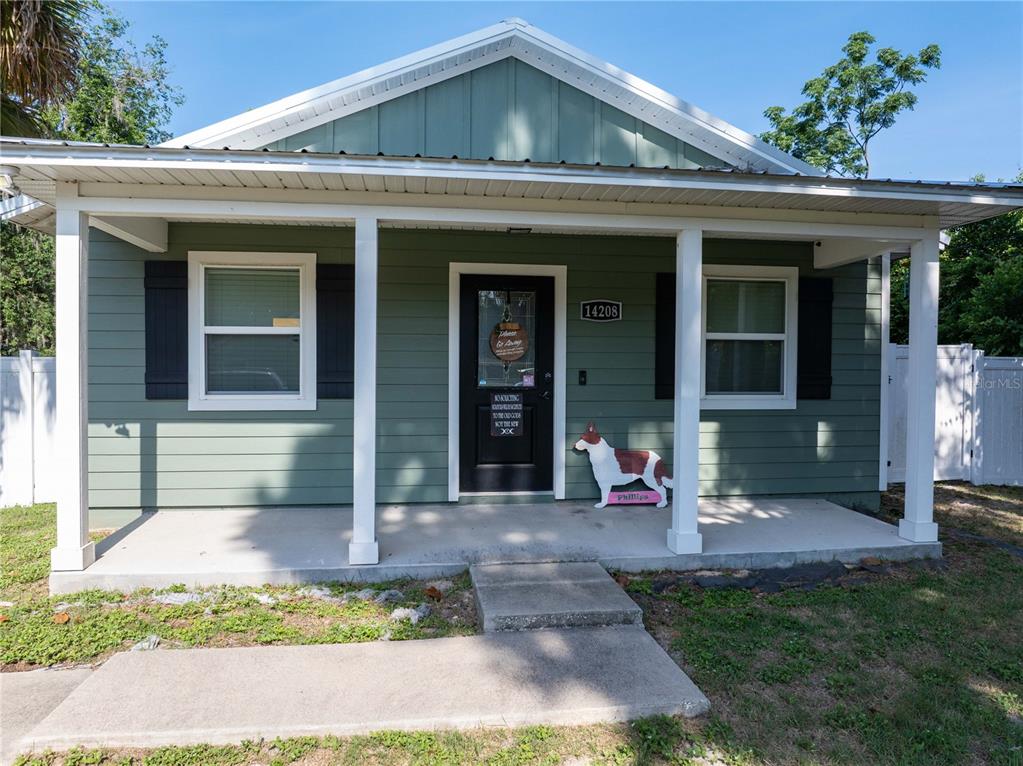 A sage green house features a front porch, white columns, and a black front door — 14208 NW 136TH TERRACE, ALACHUA, FL