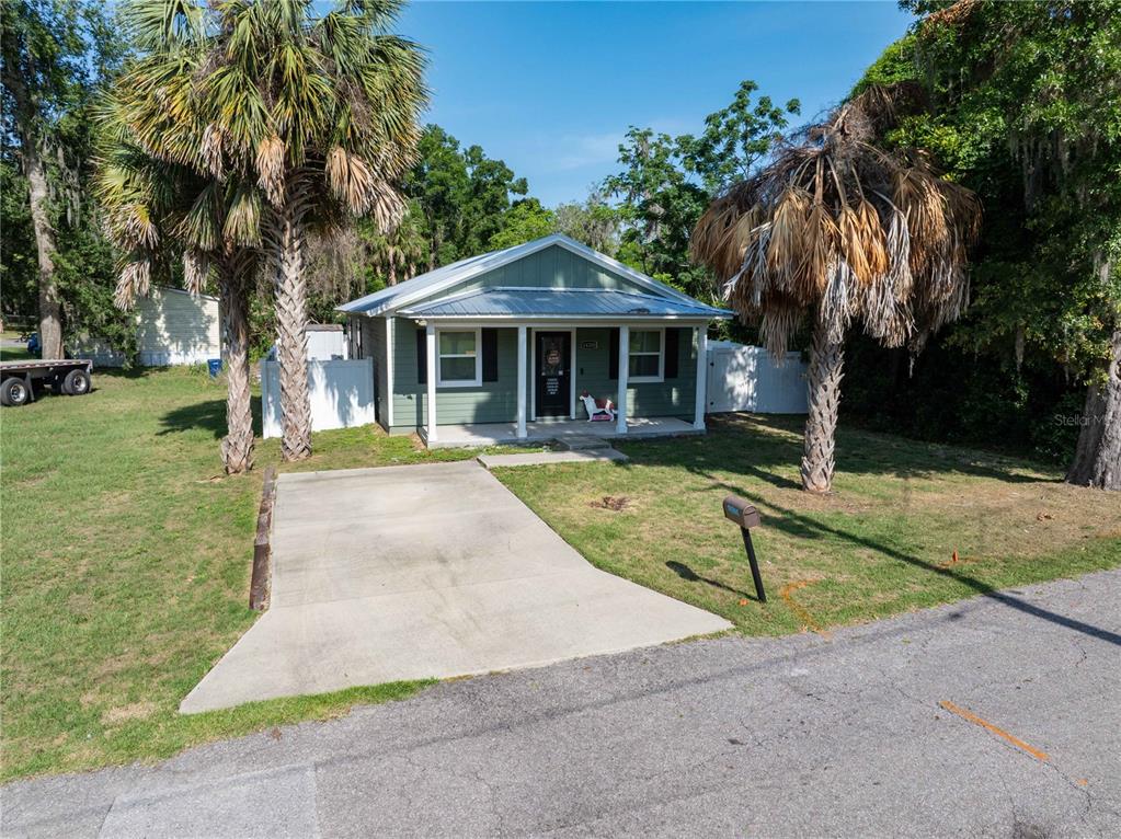 A green, single-story house with a metal roof and a concrete driveway sits outdoors — 14208 NW 136TH TERRACE, ALACHUA, FL