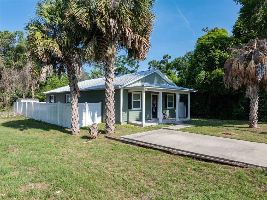 A green house with a metal roof and a front porch sits on a lawn — 14208 NW 136TH TERRACE, ALACHUA, FL