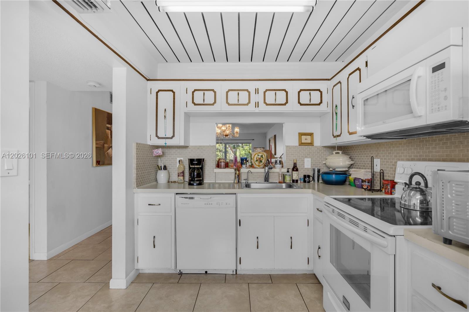 A white kitchen features a tiled backsplash, a pass-through window, and a slatted ceiling — 3551 Inverrary Dr # 208, Lauderhill FL 33319, LAUDERHILL, FL