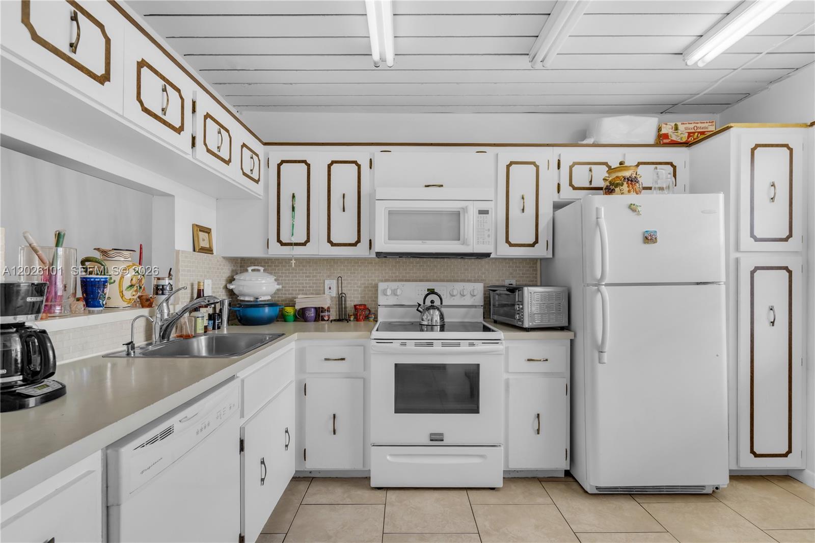 A kitchen features white cabinets with brown trim, white appliances, and a tiled backsplash — 3551 Inverrary Dr # 208, Lauderhill FL 33319, LAUDERHILL, FL