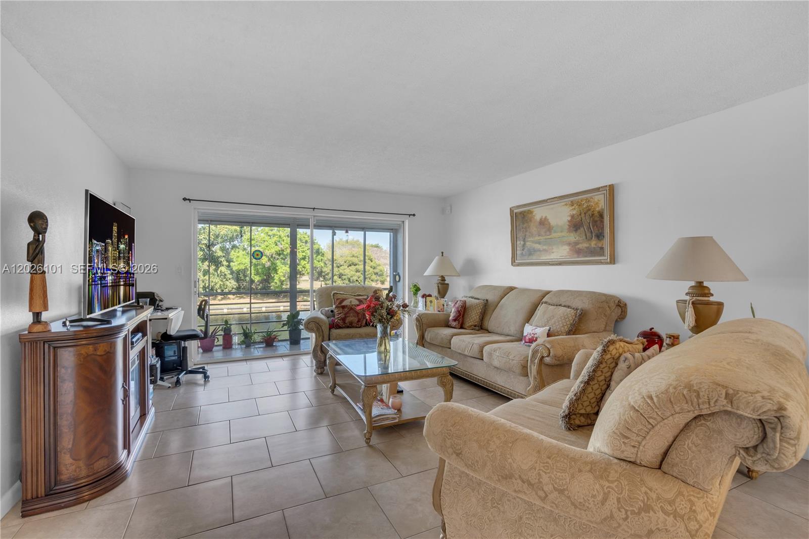 A living room features beige tile flooring, two sofas, a glass coffee table, and sliding doors — 3551 Inverrary Dr # 208, Lauderhill FL 33319, LAUDERHILL, FL