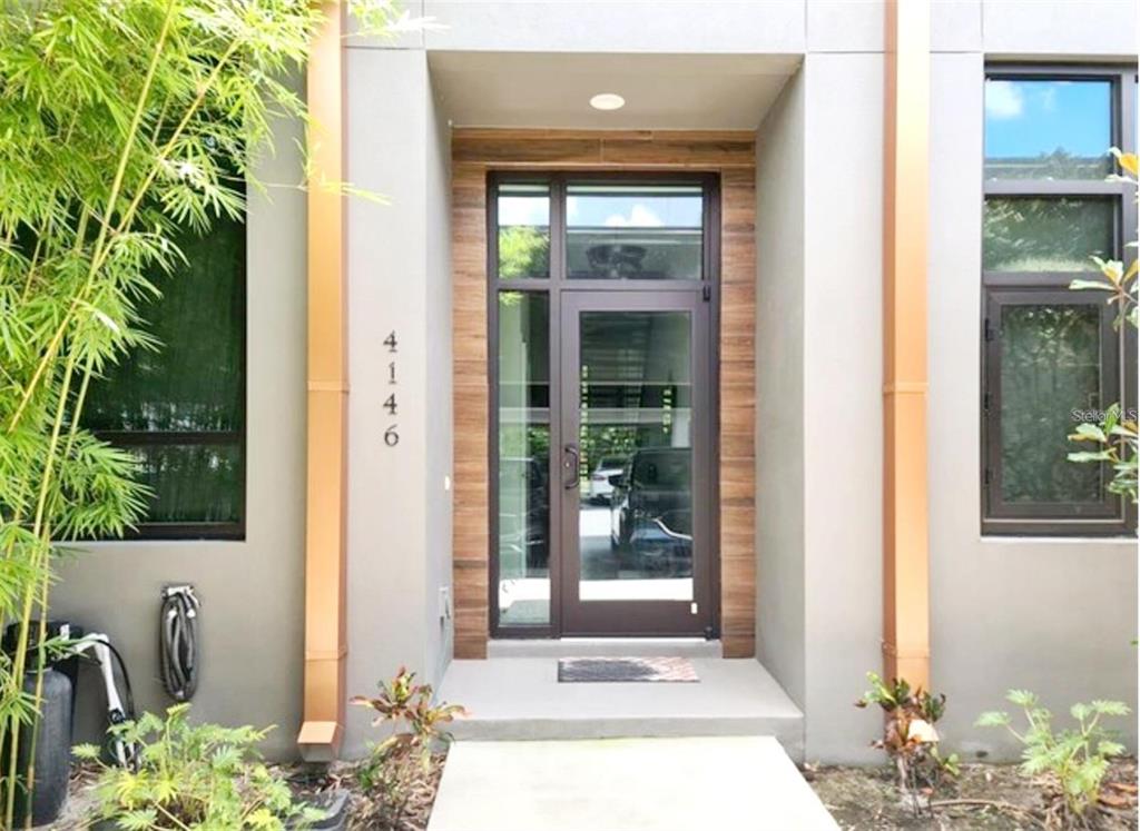 A modern home entrance features a glass door, wood-look siding, and vertical copper-colored downspouts — 4146 GAUGE LINE LOOP, TAMPA, FL