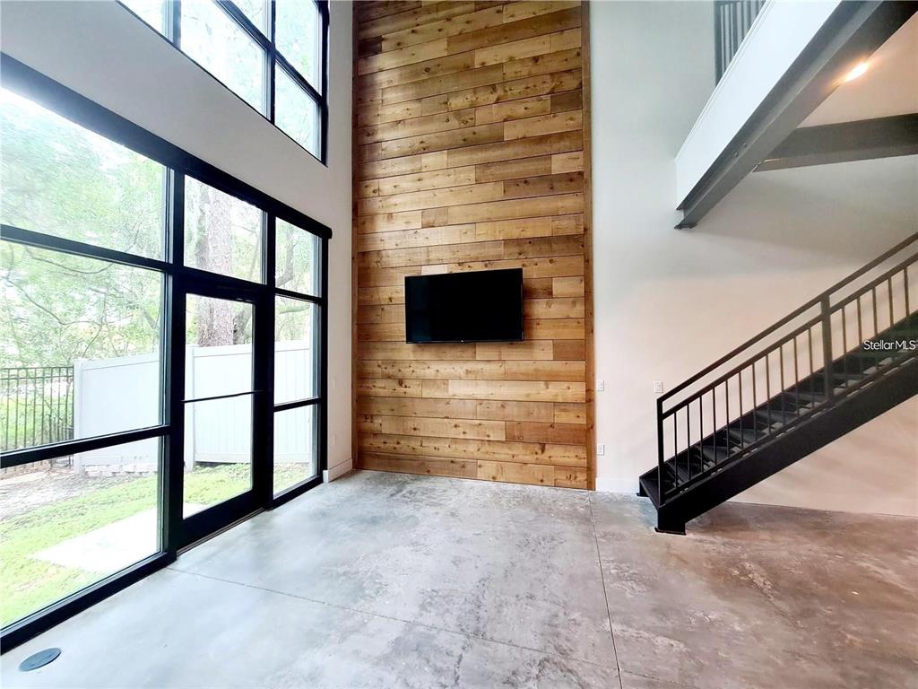 A living room features a wood-paneled accent wall, a television, large windows, and a staircase — 4146 GAUGE LINE LOOP, TAMPA, FL