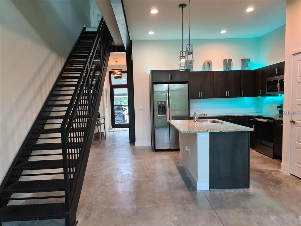 A modern kitchen with dark cabinets, a granite island, and an open metal staircase — 4146 GAUGE LINE LOOP, TAMPA, FL