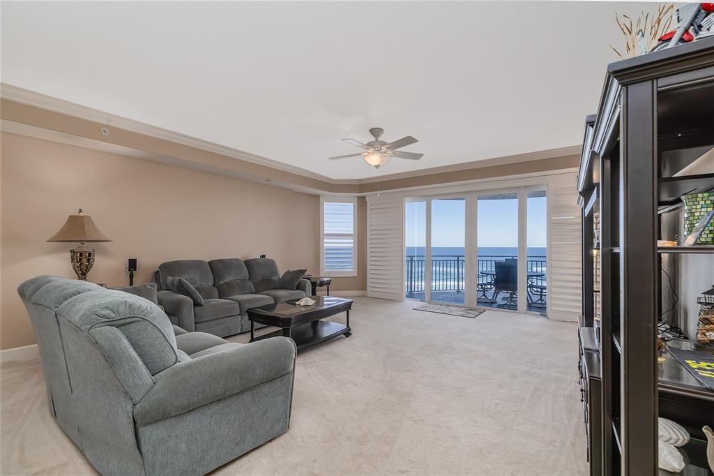A living room with gray furniture, beige carpet, and sliding glass doors overlooking the ocean — 2403 S ATLANTIC AVENUE UNIT 604, DAYTONA BEACH, FL
