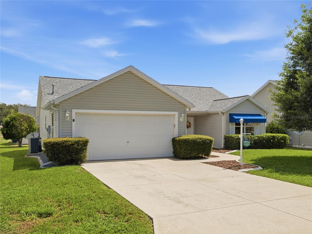 A single-story house with light siding, a two-car garage, and a blue window awning — 2707 LA POSADA DRIVE, THE VILLAGES, FL